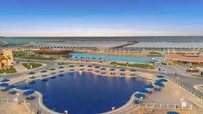 A large outdoor swimming pool with multiple lanes, surrounded by blue umbrellas and lounge chairs. - Albatros Makadi Resort (Makadi Bay)