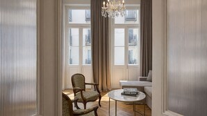 A room with a wooden chair, a round glass table with a book, a sofa, and a chandelier. - Generation 6 (Athens)