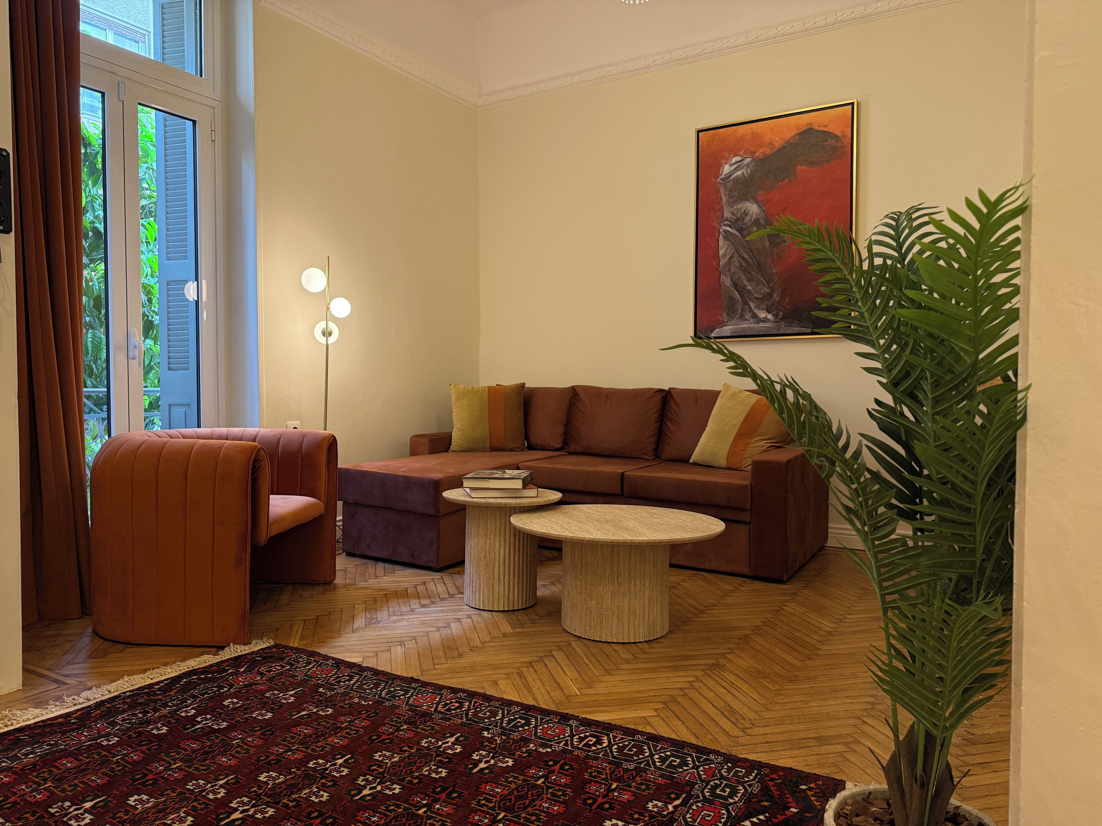 A living room with a sofa, armchair, round coffee table, and a large potted plant.