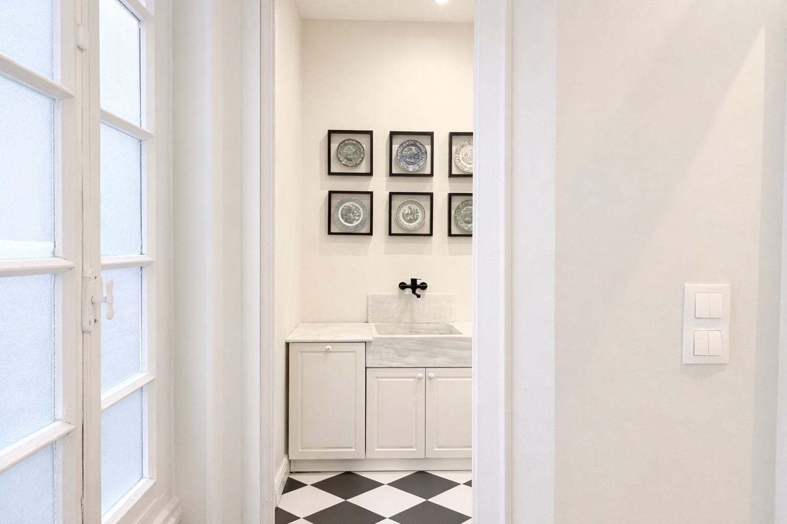 Un couloir menant à une salle de bain équipée d’un lavabo, d’un miroir et de tableaux encadrés accrochés au mur.