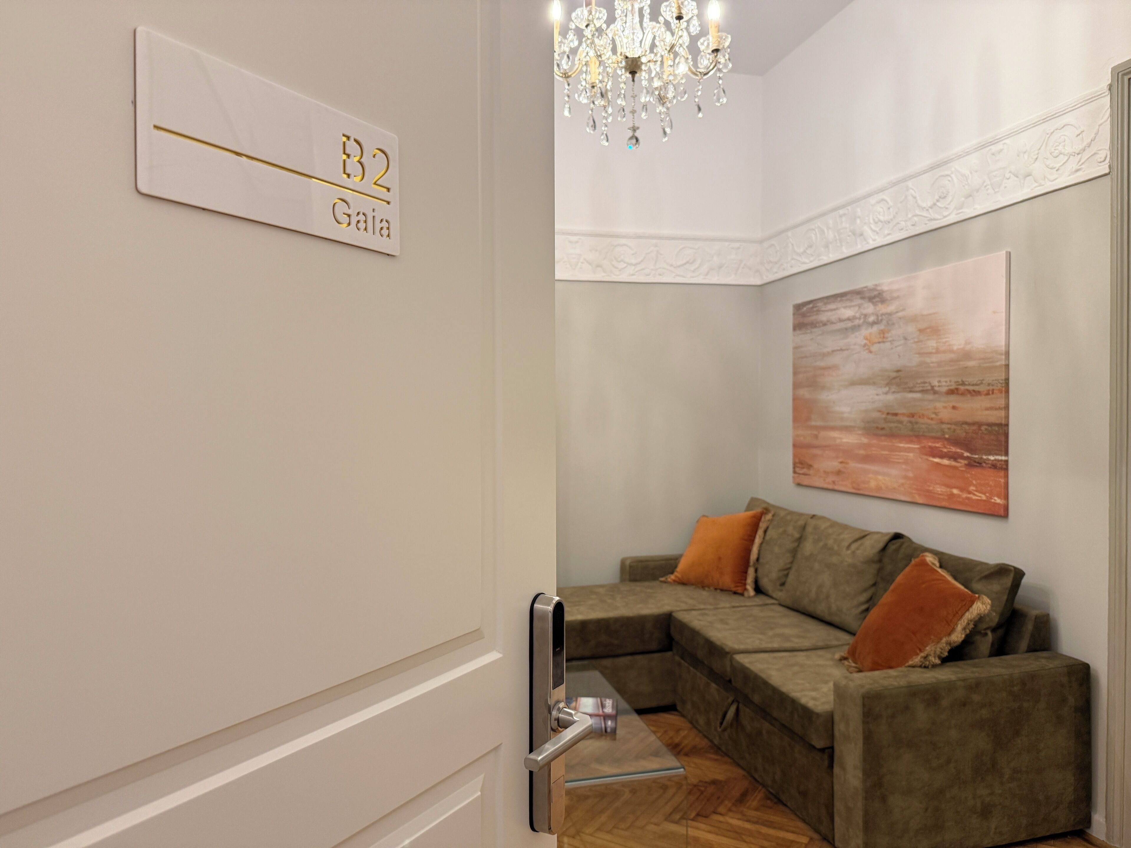 A modern interior with a sectional sofa, a chandelier, and a painting on the wall.