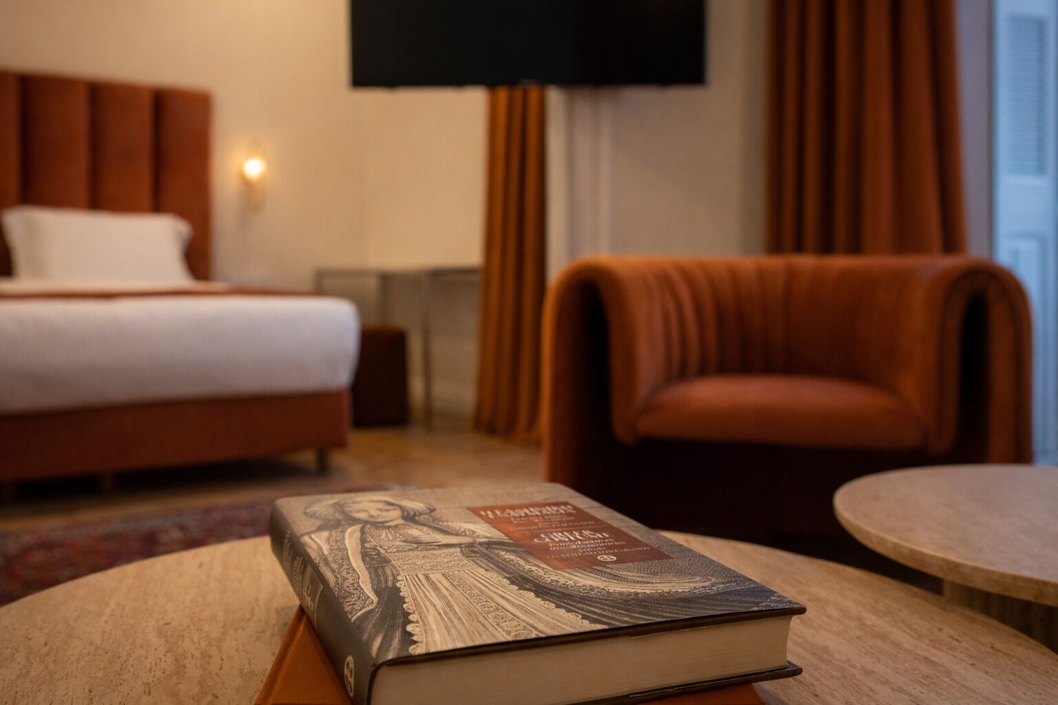 A hotel room with a bed, a chair, a round table, and a book.