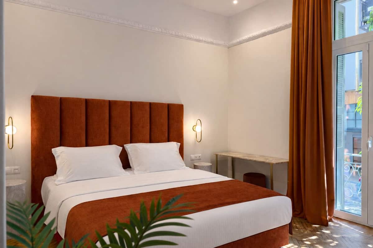 A hotel room with a bed, bedside tables, a desk, and a view of the outside.