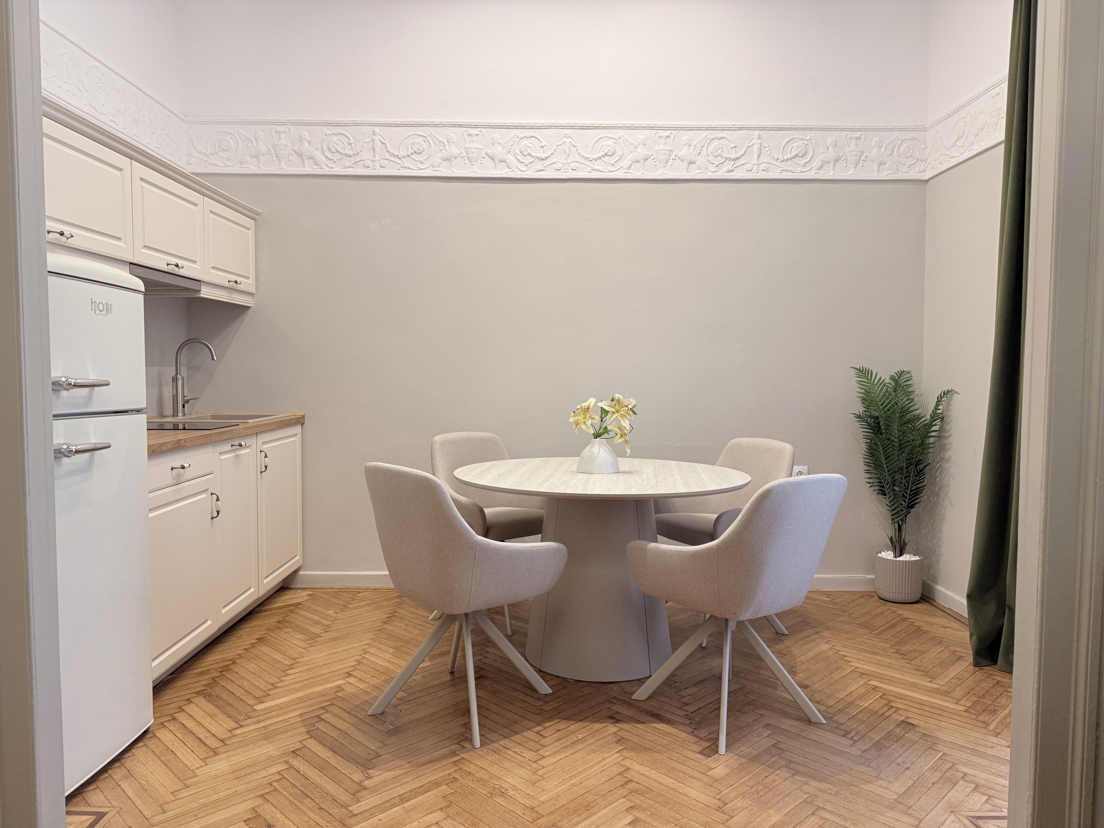 A compact kitchen with white cabinetry, a round dining table with four chairs, and a potted plant.