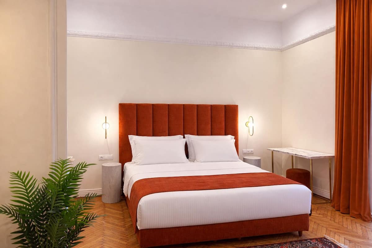 A hotel room with a large bed, two bedside tables, a desk, and a potted plant.
