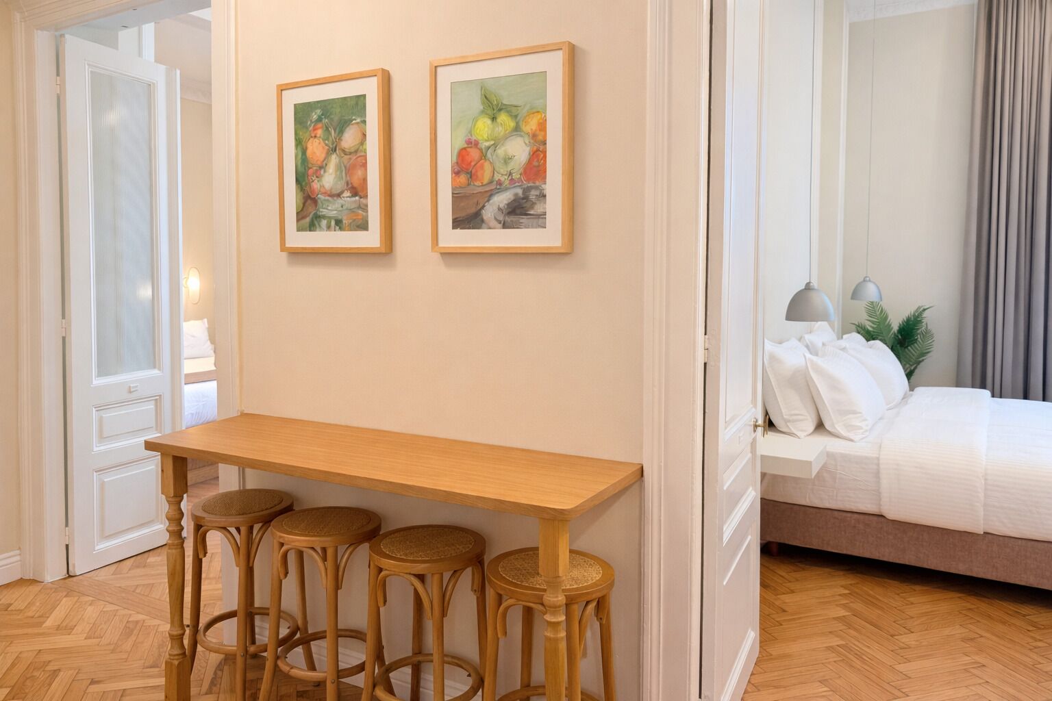 Une pièce comprenant une table en bois et quatre tabourets, un lit avec une literie blanche, et deux œuvres d’art encadrées accrochées au mur.