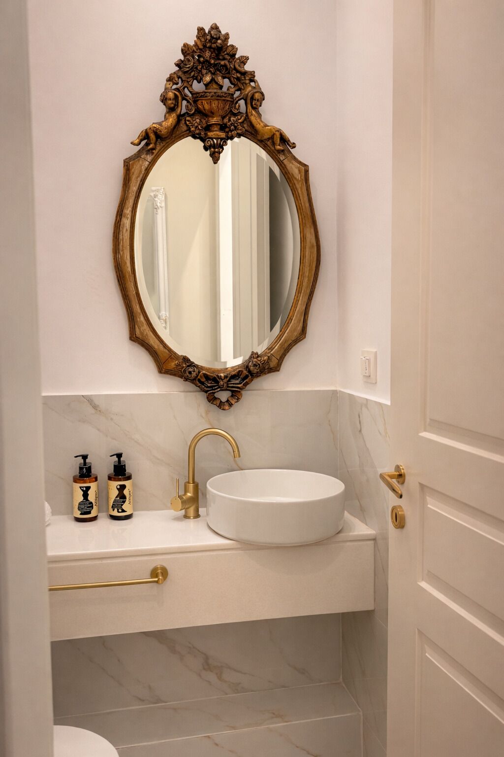 A bathroom with a marble sink, gold faucet, and a decorative mirror with cherubs.
