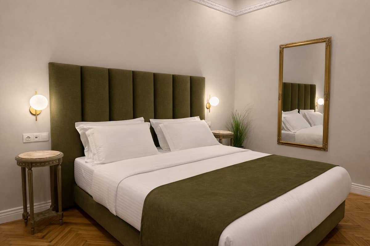 A neatly made bed with a green upholstered headboard, two bedside tables with lamps, and a large mirror on the wall.