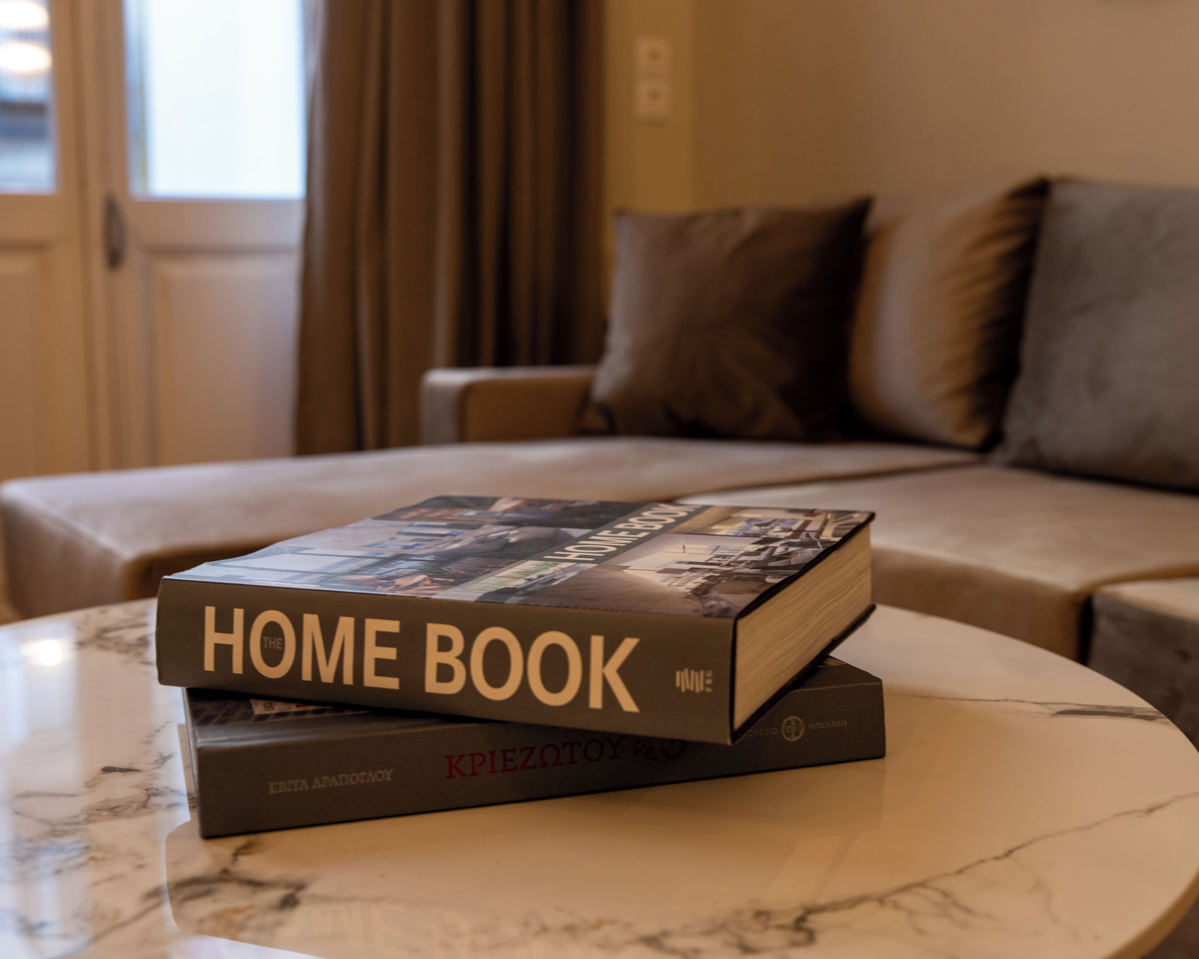 A hotel room with a bed, a sofa, and a table with a book titled 'HOME BOOK' on it.