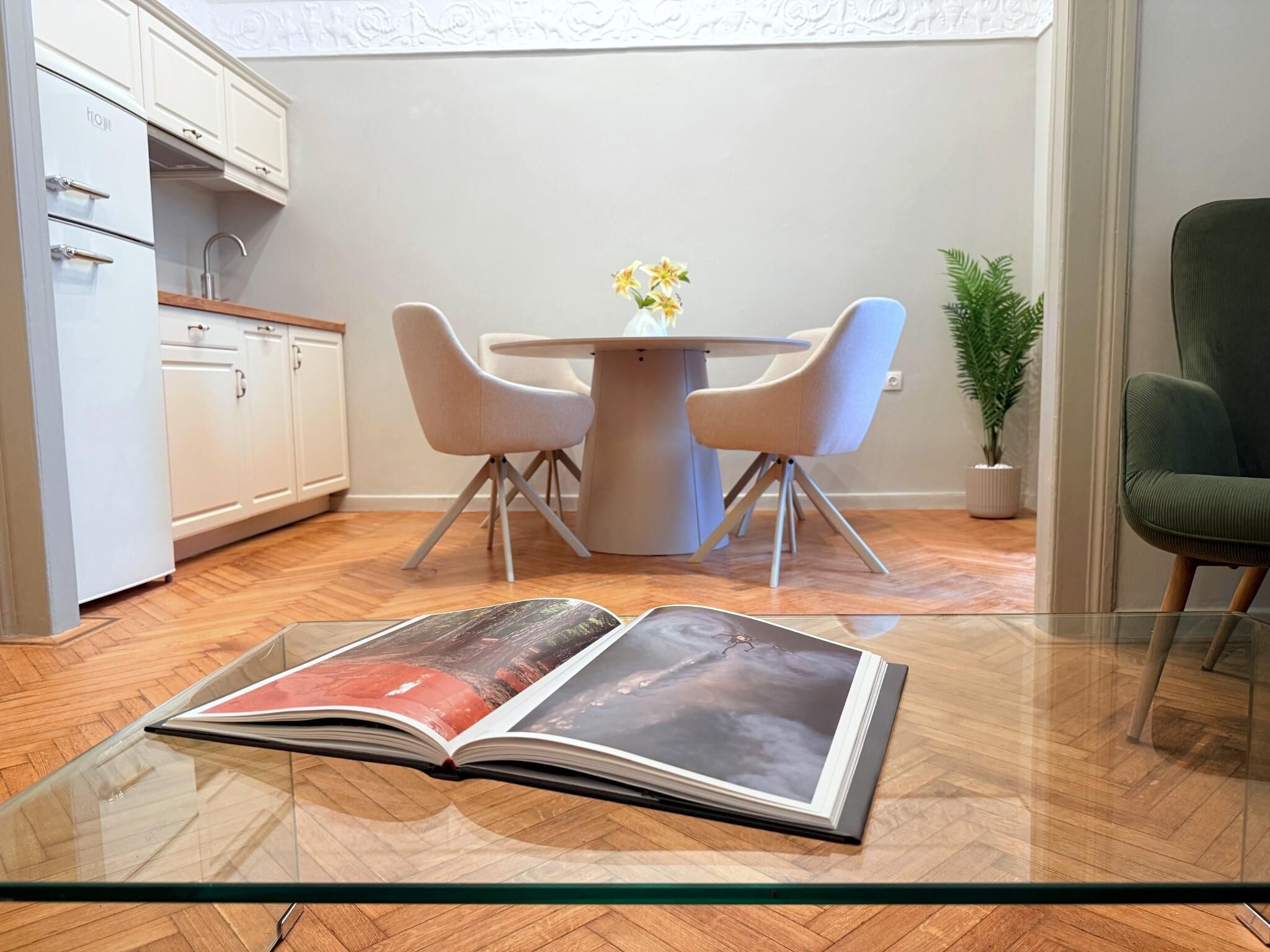 Una cucina moderna con mobili bianchi, un tavolo da pranzo con quattro sedie e una rivista su un tavolino in vetro.