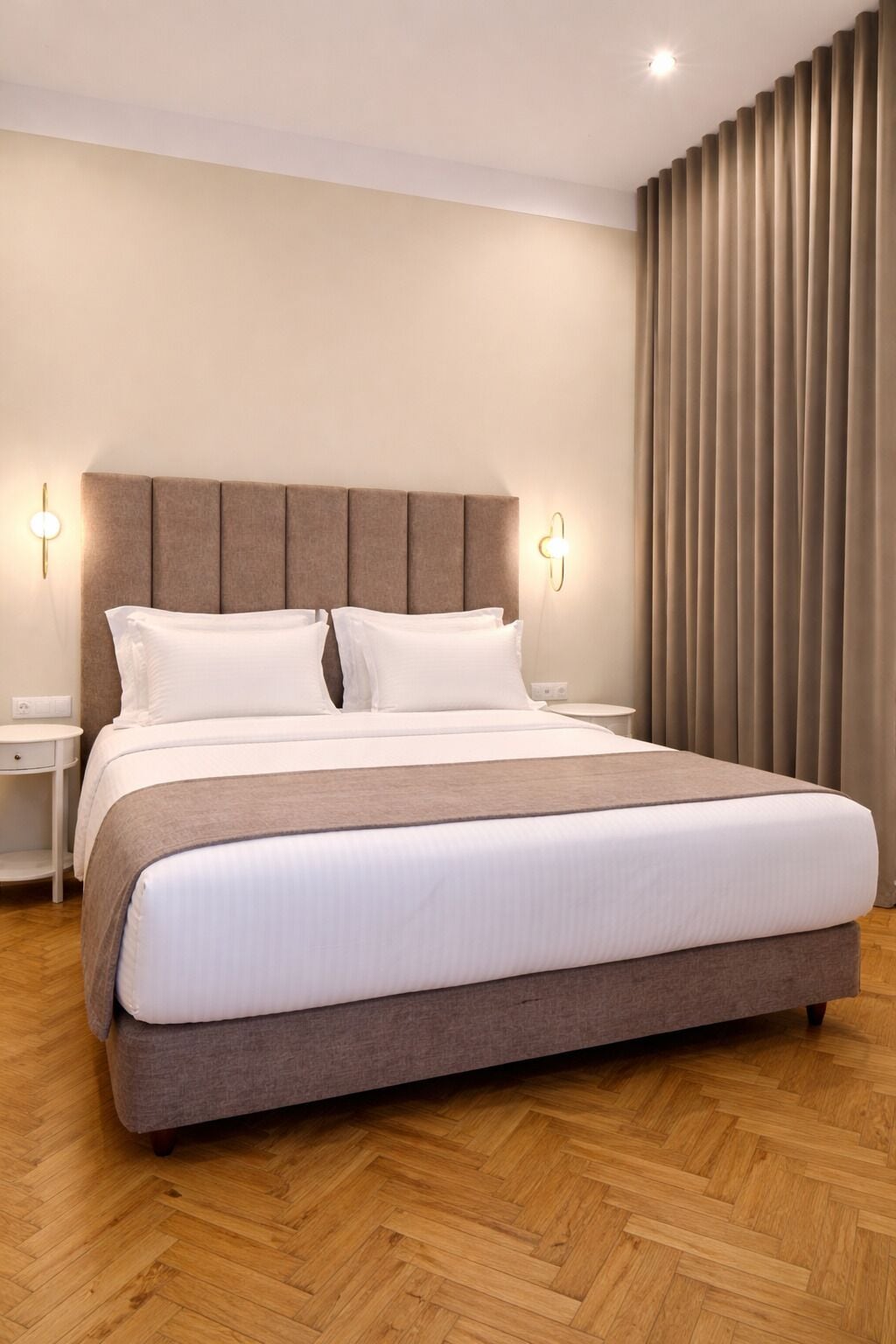 A modern hotel room with a large bed, two bedside tables, and a large window with curtains.