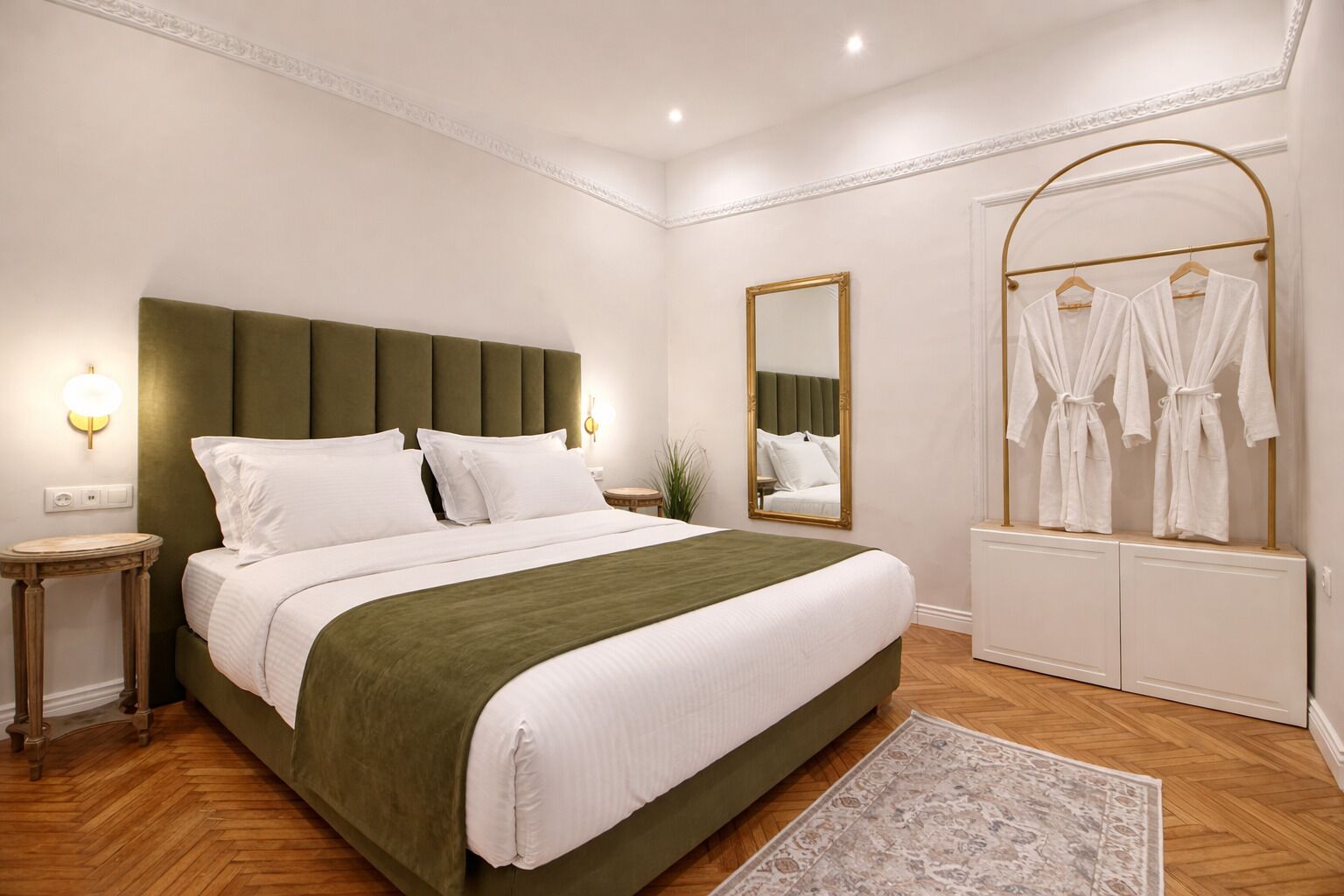 Une chambre bien rangée, avec un grand lit, des tables de chevet, un miroir et un porte-manteau.