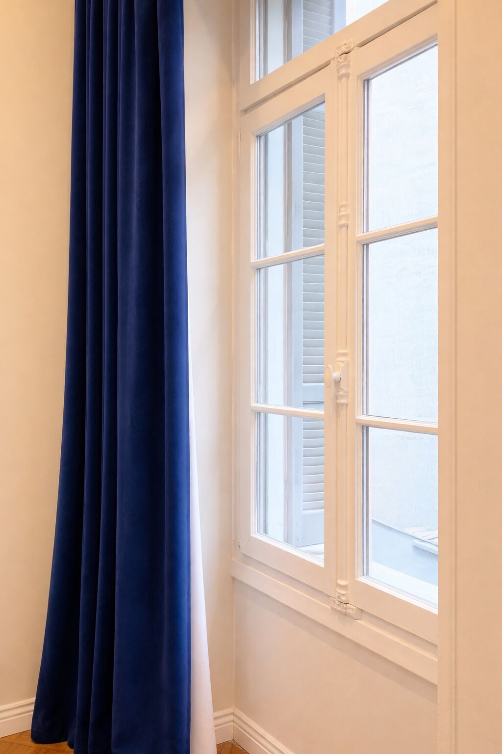 A room with a window, white walls, and a blue curtain.