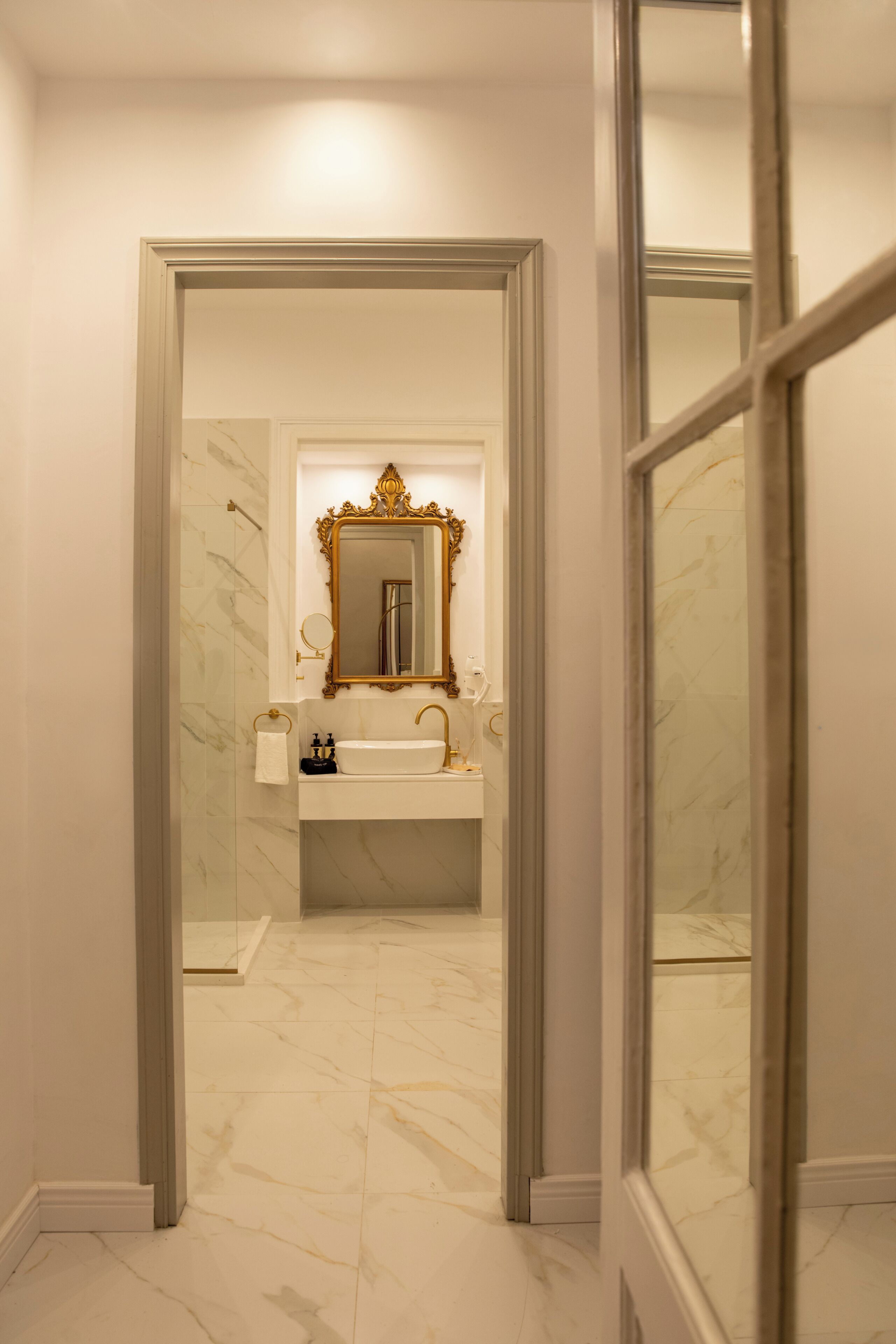 A bathroom with a marble floor, a sink, a mirror with an ornate frame, and a towel rack.