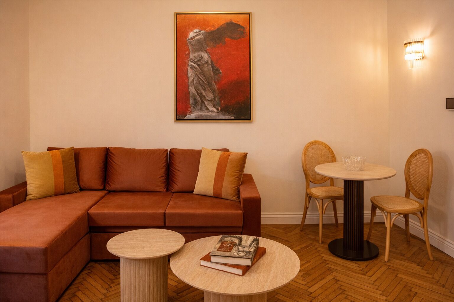 Ein Wohnzimmer mit einem braunen Sofa, zwei runden Tischen, Korbstühlen und einem gerahmten Kunstwerk an der Wand.