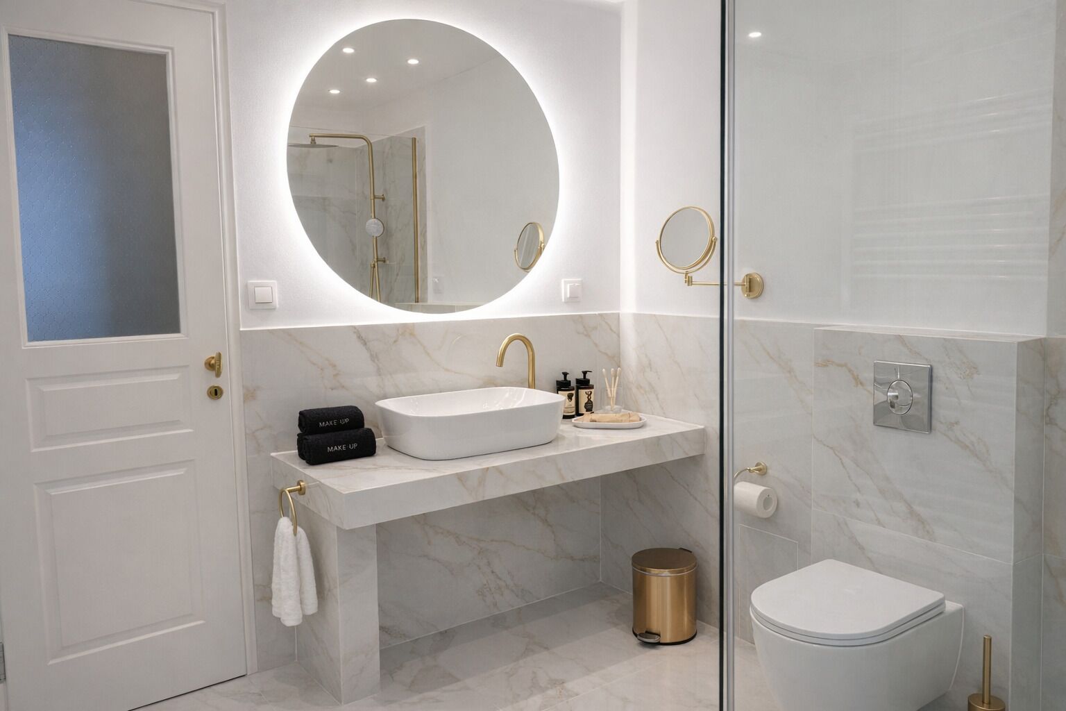 A modern bathroom with a white sink, gold fixtures, a round mirror, and a toilet.