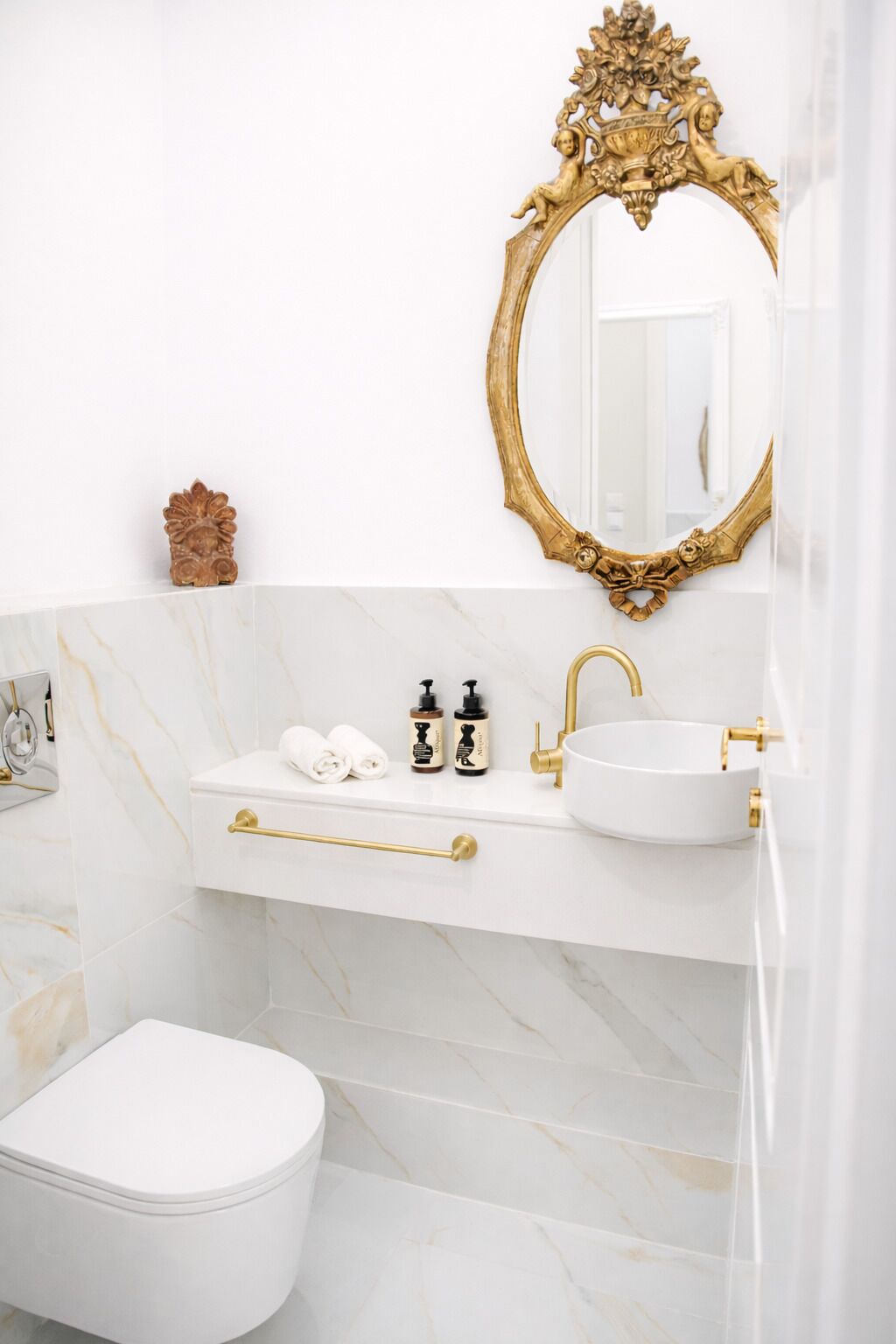 A bathroom with a white toilet, a gold-framed mirror, a white sink with gold fixtures, and marble walls.
