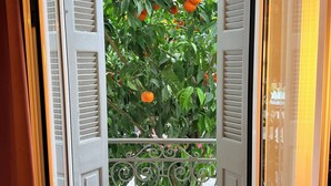 A view through an open door with a metal railing, leading to a balcony with a tree bearing fruit. - Generation 6 (Athens)