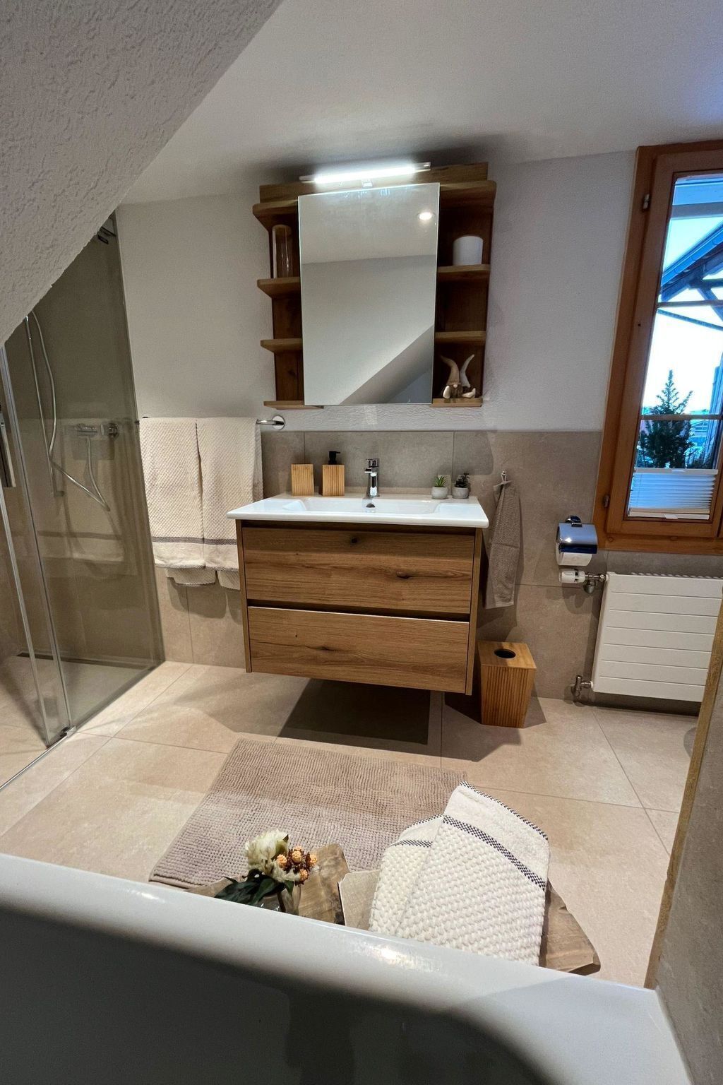 Moderni kylpyhuone, jossa on lasinen suihkuseinä, puinen pesuallas ja suuri peili.