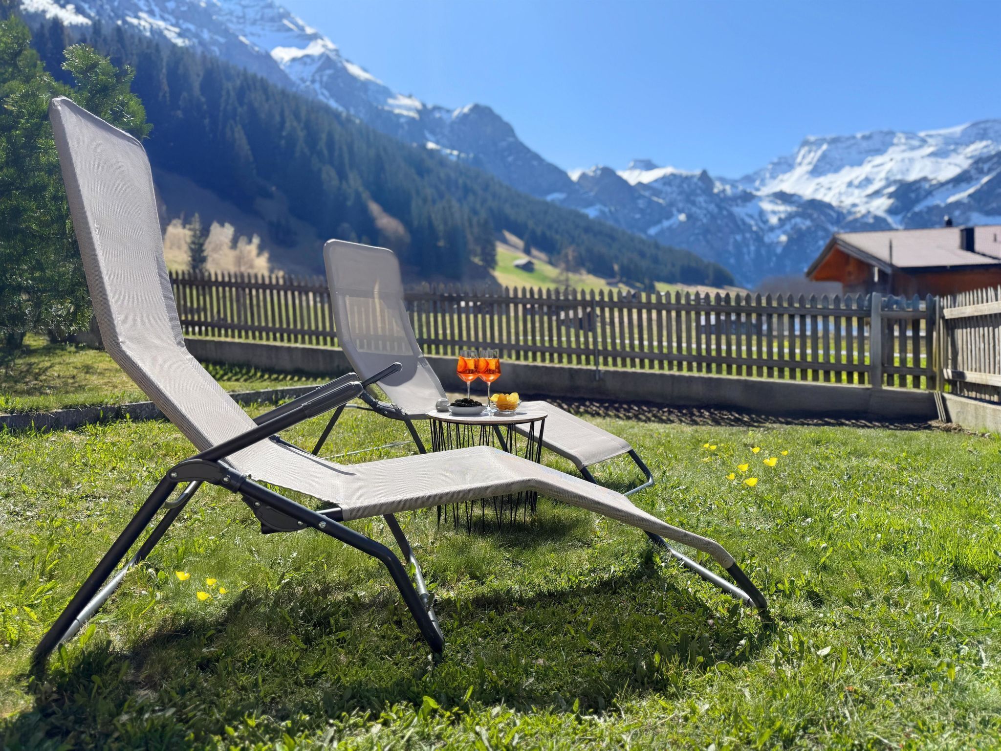 Un fauteuil confortable avec une table et des boissons, placé sur une pelouse verdoyante avec vue sur les montagnes.