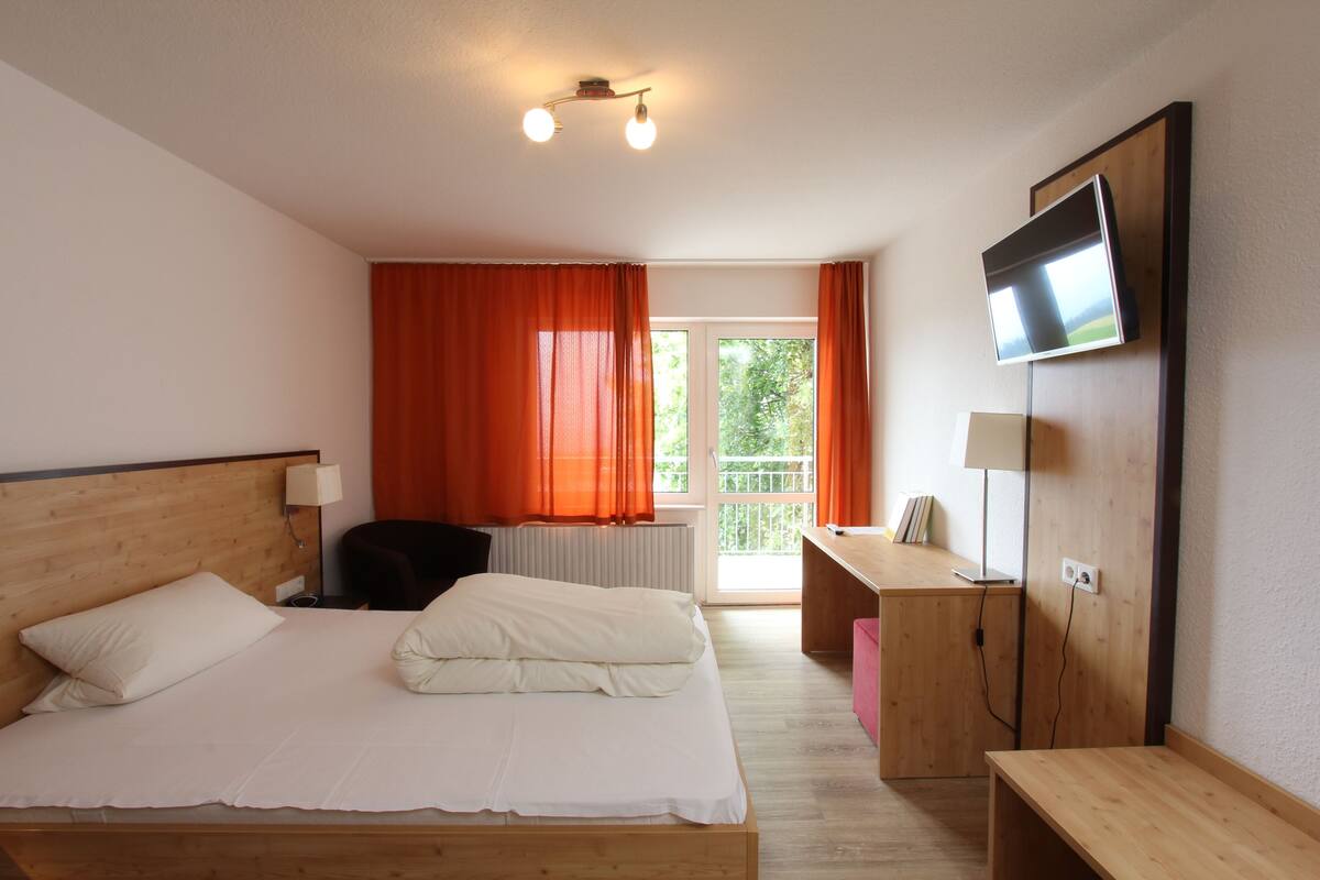 A hotel room with a bed, a desk, a chair, a TV, and a window with curtains.