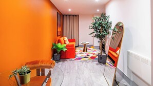 A modern living room with a wooden floor, orange walls, a red sofa, a coffee table, and a large mirror. - Cosy Bradford Apartment With City Views (Bradford)