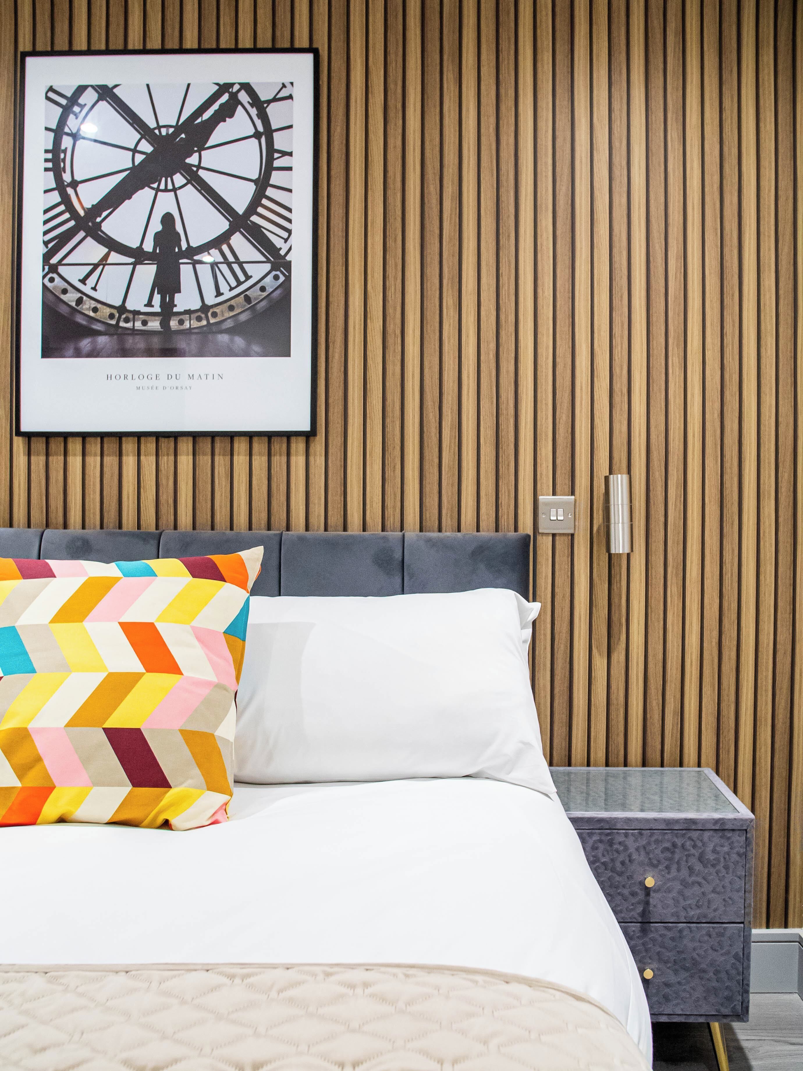 Une chambre à coucher bien rangée, avec un lit, des oreillers, une table de chevet et un tableau encadré au mur.