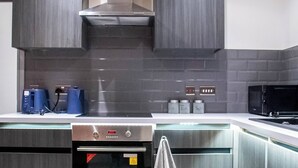 A modern kitchen with grey cabinetry, a stainless steel range hood, a built-in oven, a microwave, and a coffee machine. - Cosy Bradford Apartment With City Views (Bradford)