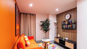 A modern living room with a vibrant orange sofa, a colorful geometric rug, a wooden wall panel, and a wall-mounted TV displaying movie posters. - Cosy Bradford Apartment With City Views (Bradford)