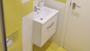 A small bathroom with a white sink, yellow and white tiles, a toilet, and a door.
