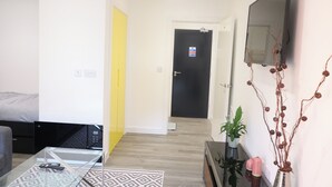A modern living room with a glass coffee table, a sofa, a TV mounted on the wall, and a door leading to another room.