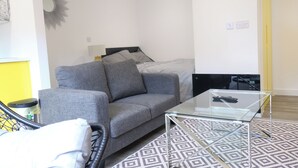 A modern living room with a grey sofa, a glass coffee table, and a patterned rug.