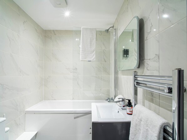A modern bathroom with a bathtub, a glass-enclosed shower, a vanity with a mirror, and a towel rack.