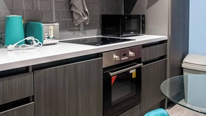 A modern kitchen with a stainless steel range hood, a microwave, and a built-in oven. There is a glass table and a teal chair. - Bradford City Apartment - Bolton Road Oasis (Bradford)