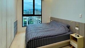 Une chambre à coucher moderne avec un grand lit, une table de chevet et une vue sur la ville par la fenêtre.