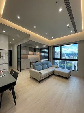 A modern living room with a sectional sofa, a dining table, and a view of a cityscape through large windows.
