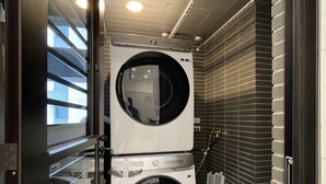 Une petite buanderie équipée de deux machines à laver à chargement frontal superposées, d’un sol carrelé et d’un radiateur en métal.