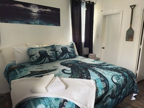 A bed with an octopus-themed duvet, a night sky painting, a door with a number plate, and a wall-mounted shovel.