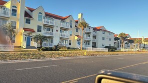 A row of multi-story buildings with balconies, a clear sky, and a road in the foreground.
