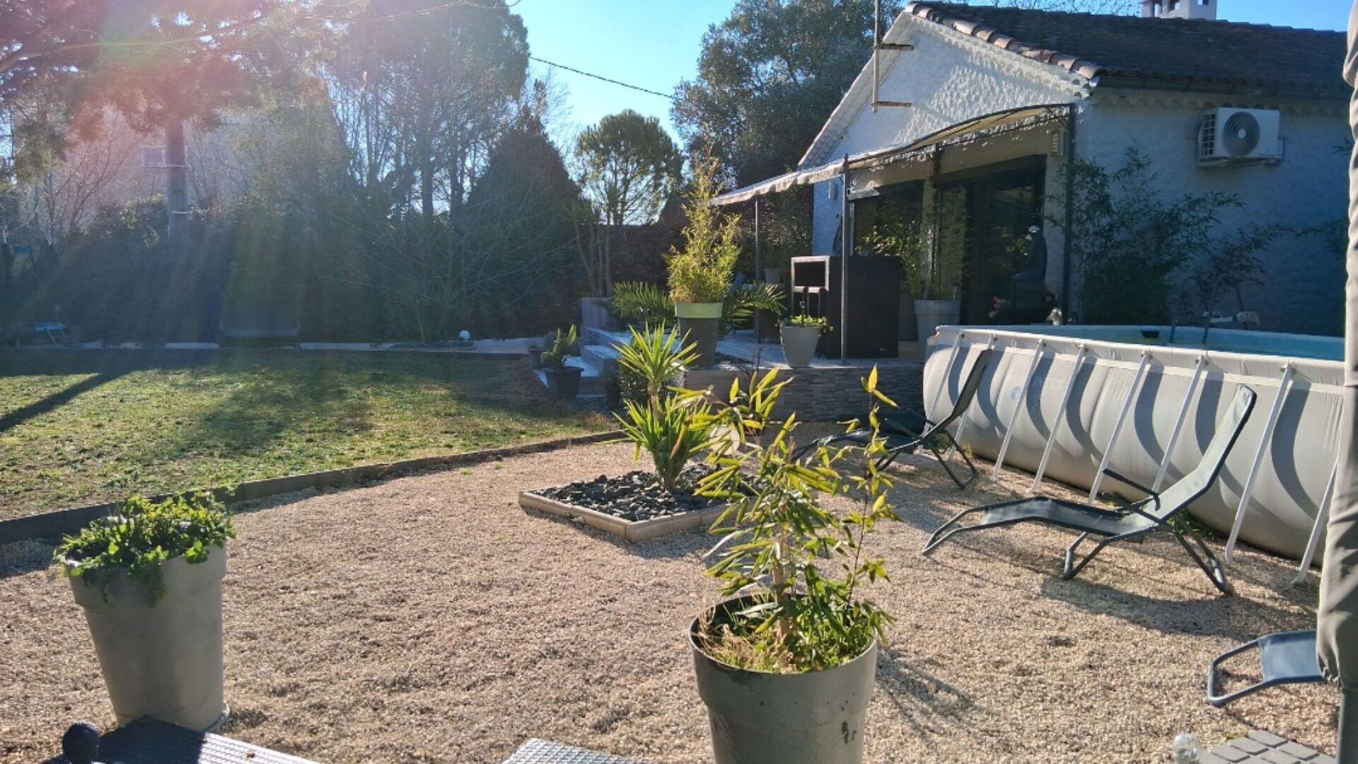 Een terras met buitenmeubilair, een kleine tuin met potplanten, en een gebouw met een pannendak op de achtergrond.