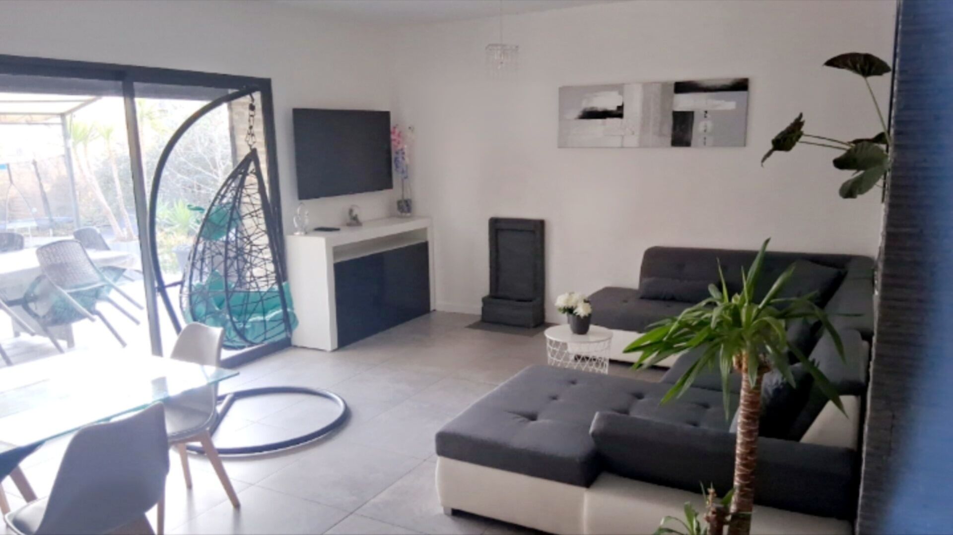 A modern living room with a sofa, a dining area with chairs, a TV, and a plant.
