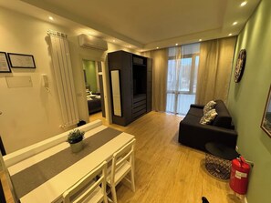 A modern living room with a sofa, a dining area with a table and chairs, and a kitchen in the background. - Vatican Apartment D2 - 2 min. from the Valle Aurelia Metro Station, Wi-Fi, and air conditioning (Roma)