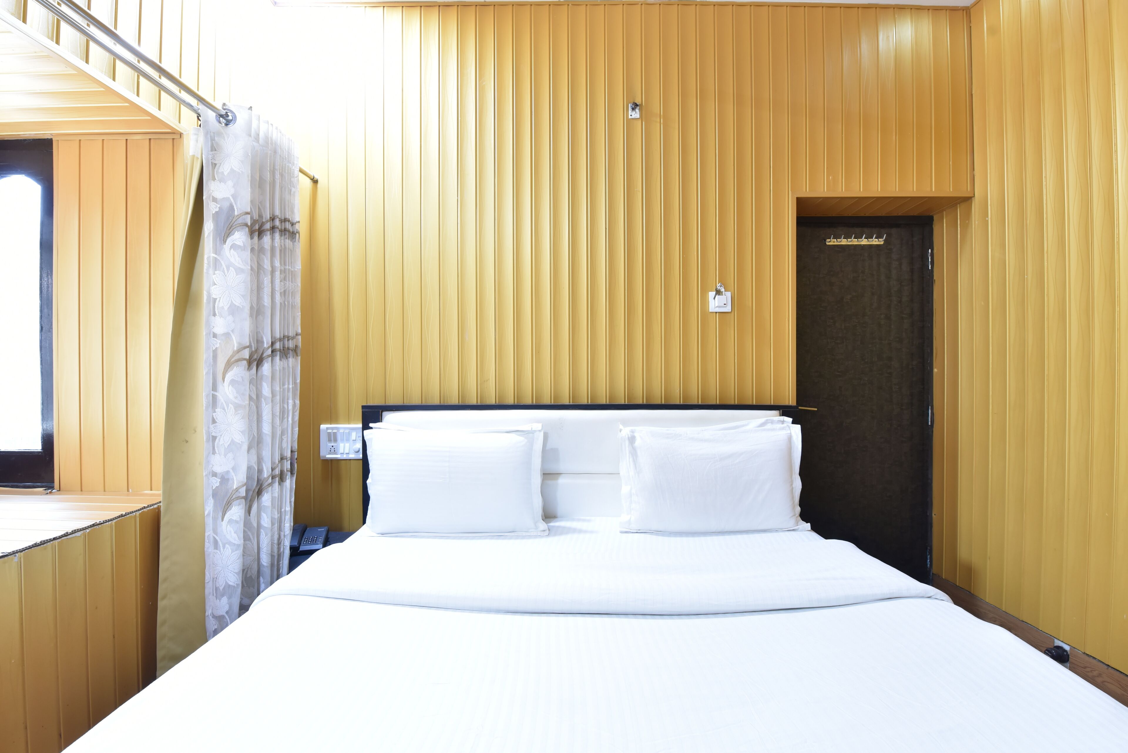 Quarto de hotel com uma cama grande, parede de madeira, uma porta e uma janela.