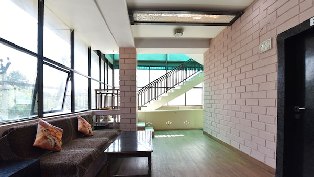 A spacious lobby with a wooden floor, a brown sofa with decorative pillows, a small table, and a staircase leading to an upper level.