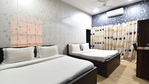 A hotel room with two beds, a ceiling fan, an air conditioning unit, and a curtain with a floral pattern.