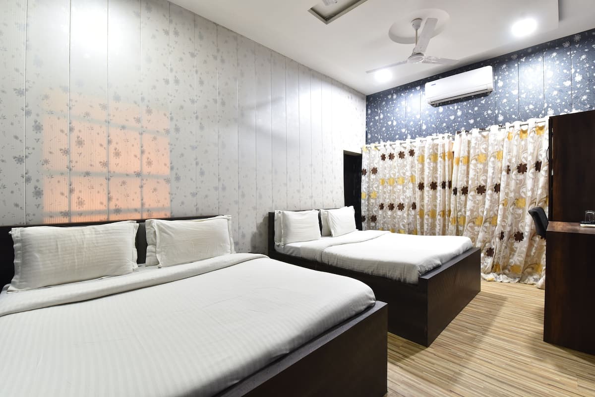 Hotellihuone, jossa on kaksi sänkyä, kattotuuletin, ilmastointilaite ja kukkakuviollinen verho.