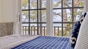 Un dormitorio con un ventanal grande, una cama con cabecera estampada y vistas a árboles y una masa de agua.