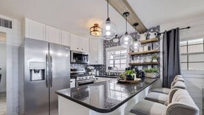 Una cocina moderna con una isla central, electrodomésticos de acero inoxidable e iluminación colgante.