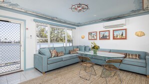 Una sala de estar con un sofá azul, una mesa de centro de vidrio y vistas al exterior a través de amplios ventanales.