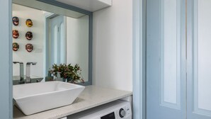 Un baño con un lavamanos grande de color blanco, un espejo y un inodoro fijado a la pared.